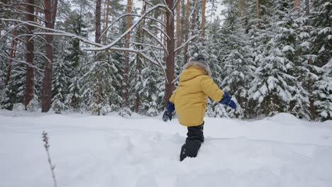 A-boy-in-a-yellow-jacket-walks-through-deep-snow-studying-the-winter-forest-winter-walks-and-through-the-snow-forest-in-slow-motion.-The-concept-of-a-free-environment-for-children